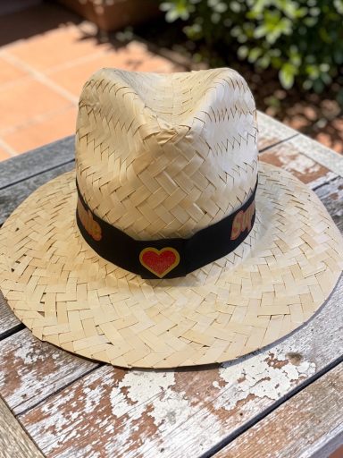 Chapeau en paille avec un bandeau noir et un cœur en motif, posé sur une table en bois.